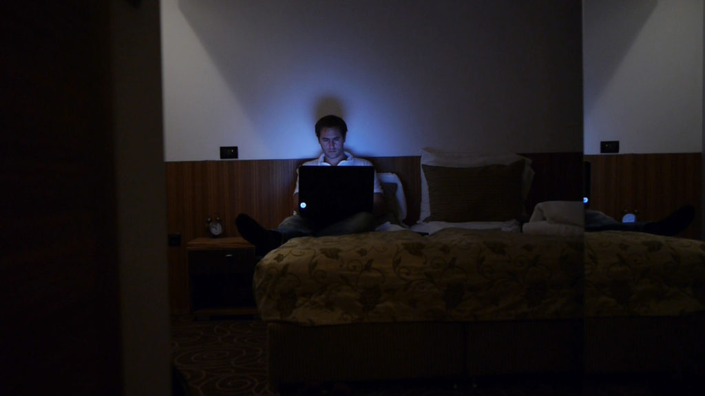 Man at laptop in hotel bed at night